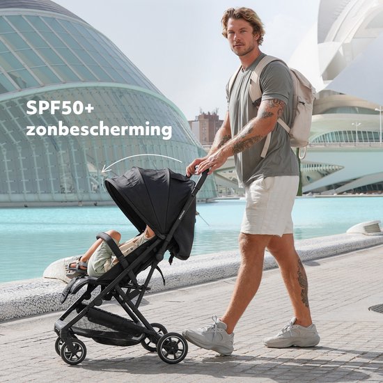 Man duwt zwarte Deryan buggy met kind op een zonnige promenade.