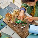 Een jongen met een bril bouwt aan een LEGO leeuw op een tafel. Naast de leeuw liggen LEGO stenen en een tablet.