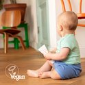 Baby zit op de vloer met een Naïf tube in zijn hand, kijkt naar de zijkant. Vegan logo zichtbaar.