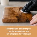Een persoon met zwarte handschoen poetst een houten snijplank op met een doek.