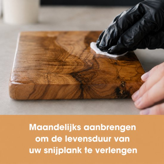Een persoon met zwarte handschoen poetst een houten snijplank op met een doek.