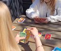 Twee personen aan een houten tafel spelen een kaartspel met afbeeldingen van voetballers.