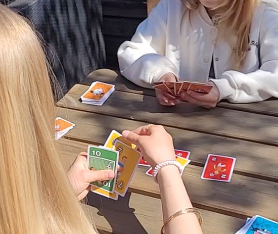 Twee personen aan een houten tafel spelen een kaartspel met afbeeldingen van voetballers.