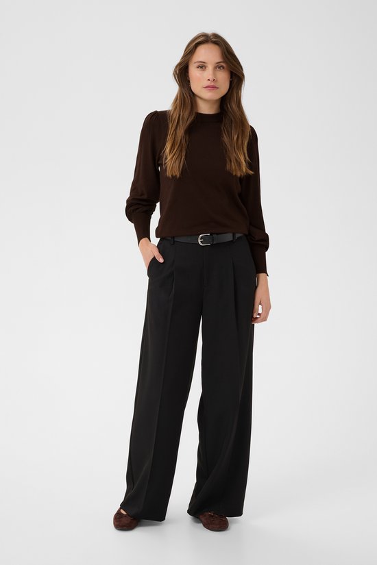 Model in bruine trui met pofmouwen en zilverkleurige knopen, gecombineerd met wijde zwarte broek.