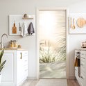 Deurposter met zandduinen en grassprieten bij zonsondergang, in een keuken met witte kasten.