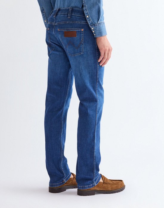 Zijaanzicht van een man in blauwe Wrangler jeans en spijkerhemd.