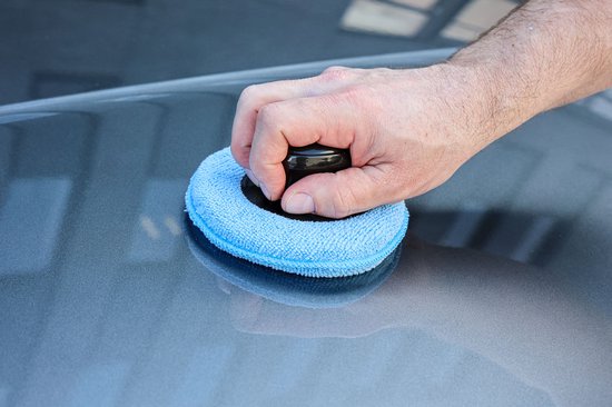 Hand met een Protecton polijstpad met blauwe microvezel pad, die op een auto wordt gebruikt.