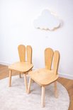 Twee houten kinderstoeltjes met konijnenoren op een wit kleed, met een wolk lamp aan de muur.