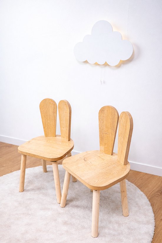 Twee houten kinderstoeltjes met konijnenoren op een wit kleed, met een wolk lamp aan de muur.