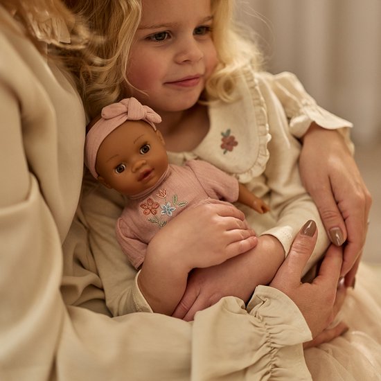 Kind houdt een babypop Yara vast in roze outfit met bloemenborduursel.