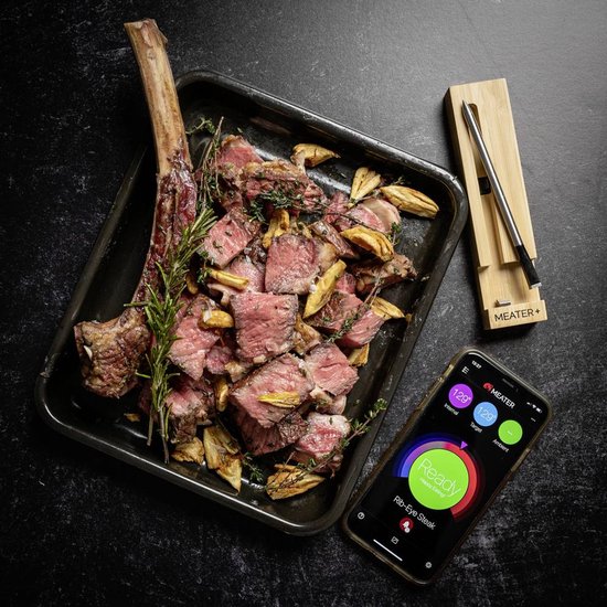 Een grote Tomahawk steak, gesneden, op een bakplaat met een Meater+ thermometer en een app op de telefoon.