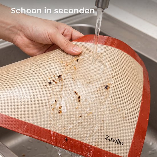 Een hand die een vervuilde Zavillo bakmat schoonspoelt onder stromend water.