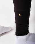 Détail de la cheville d'un legging thermique noir avec un trèfle doré.