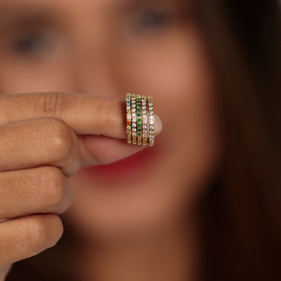 Vrouw toont stapelbare gouden ringen met gekleurde zirkonia's.