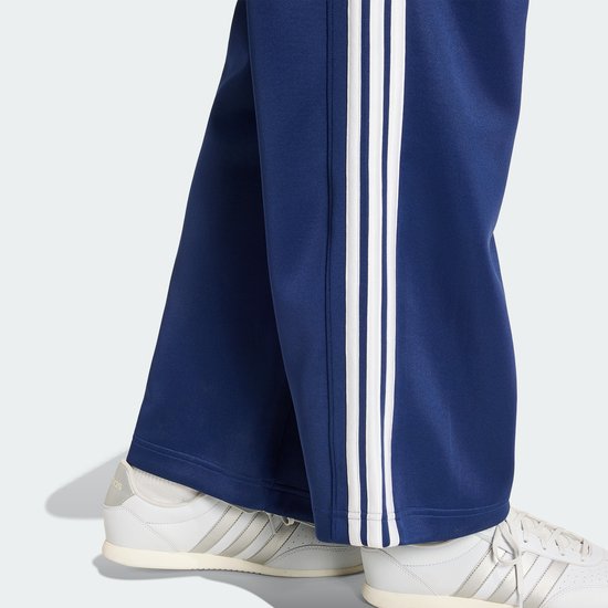 Donkerblauwe trainingsbroek met witte strepen op de zijkanten, gedragen met witte sneakers.