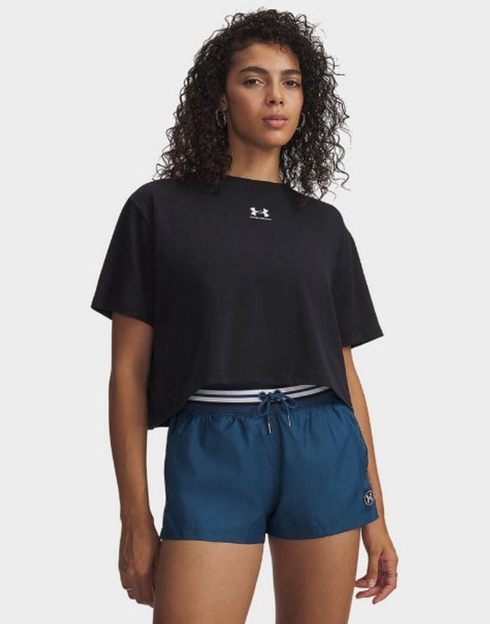 Model draagt een zwarte, cropped Under Armour T-shirt met wit logo en blauwe shorts met gestreepte tailleband.