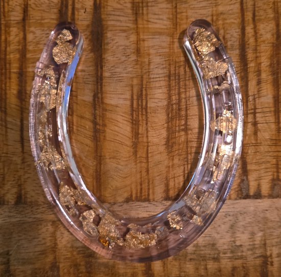 Hoefijzer gegoten in epoxy met gouden vlokken, op een houten ondergrond.