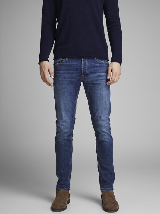 Man in donkerblauwe trui en blauwe jeans, deels in beeld.
