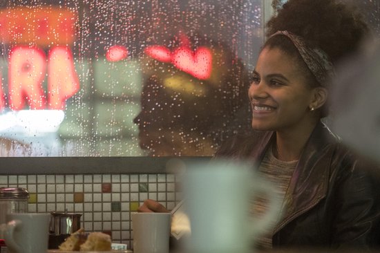 Vrouw met afro-kapsel en hoofdband glimlacht in een restaurant bij regenachtig weer.