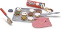 Houten koekjes op bakplaat met rode ovenwant, spatels en rol koekjesdeeg. Koekjes met sprinkles, chocolade, groene en blauwe icing, polka dots.
