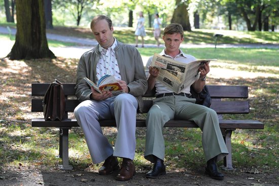 Twee mannen lezen in een park op een bankje, één leest een boek, de ander een krant.