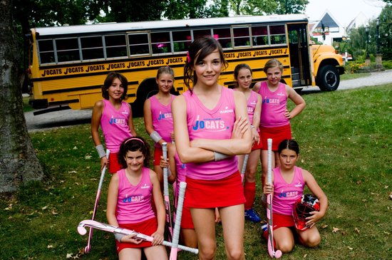 Team van meisjes in roze tenues met 'JO CATS' op een grasveld.