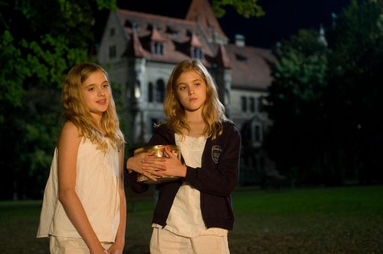Twee blonde meisjes in witte kleding staan buiten bij een kasteel.