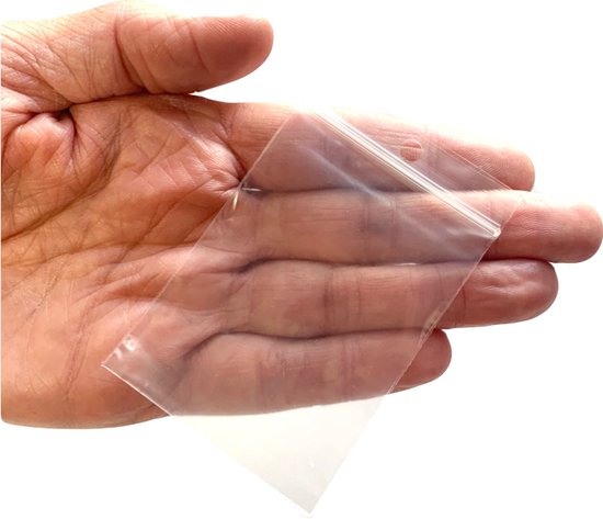 Een hand houdt een klein, doorzichtig, plat gripzakje van 8x6cm met ziplock sluiting open.