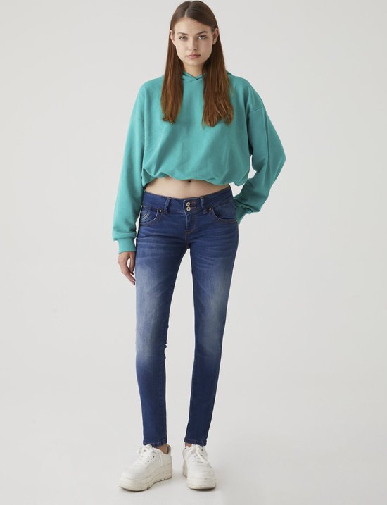 Een vrouw in een cropped turquoise hoodie en een nauwsluitende blauwe jeans, met witte sneakers.