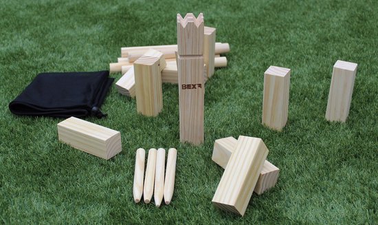 Een houten koningsstuk met de tekst BEX, staand op kunstgras met andere Kubb-blokken, stokken en een zwart zakje.