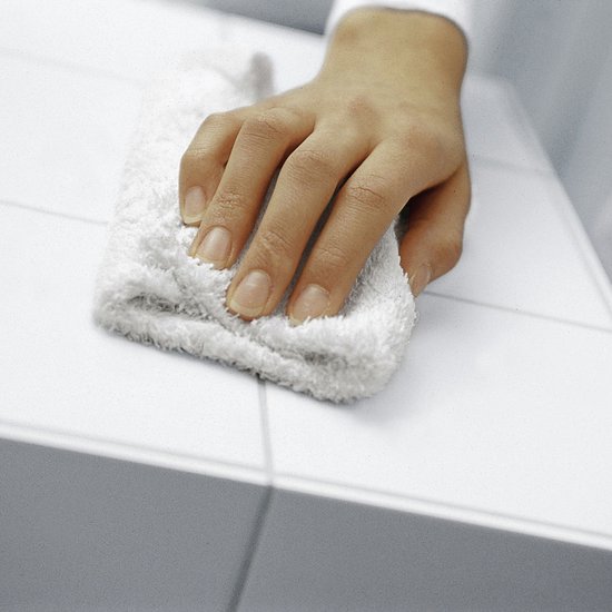 Hand veegt met een witte badstof doek over een witte tegel.