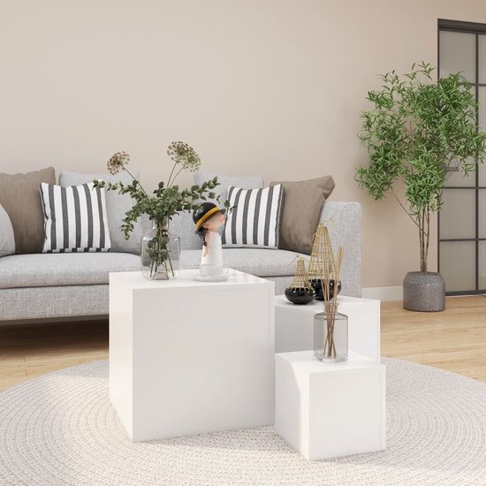 Drie witte kubusvormige bijzettafels op een rond vloerkleed voor een grijze bank met gestreepte kussens.