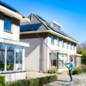 Man met telescoopsteel met borstel aan het schoonmaken van een huis met zonnepanelen.