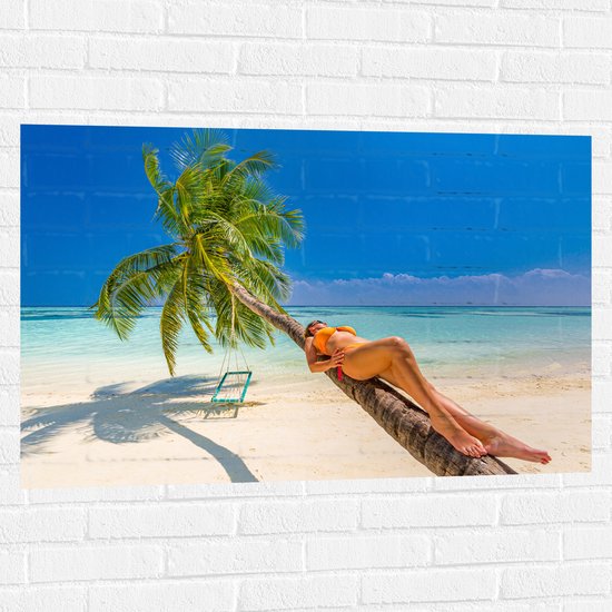 Muursticker - Vrouw in Gele Bikini Liggend op Schuingroeiende Palmboom op Tropisch Strand - 105x70 cm Foto op Muursticker