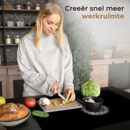 Vrouw snijdt komkommer op inductiebeschermer met paardenbloemprint in een keuken.
