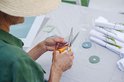 Oranje Fiskars schaar wordt gebruikt om rond grijs papier te knippen, met een vrouw met strooien hoed.