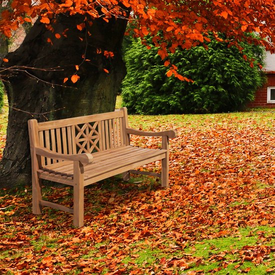 Teakhouten tuinbank met decoratief rugpatroon, geplaatst onder een boom met oranje bladeren in de herfst.