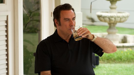 Een man met zwart haar, een zwart poloshirt, drinkt uit een glas met een gouden horloge om zijn pols.