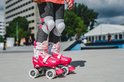 Kind met roze rolschaatsen aan, grijze jeans en beschermers op een betonnen ondergrond.