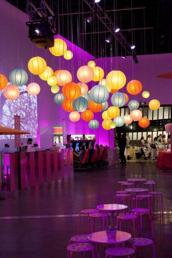 Veelkleurige lampionnen verlichten een feestzaal met tafels en stoelen.