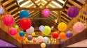 Veelkleurige lampionnen hangen op een zolder met houten balken.