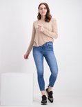 Vrouw met lang bruin haar, draagt een beige trui met lange mouwen en blauwe skinny jeans, luipaardprint sneakers.