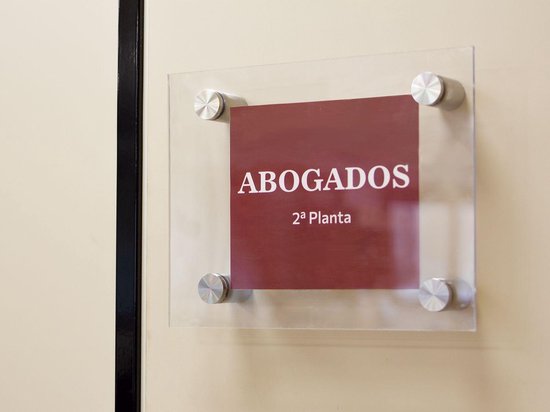 Bravos reclamebord met tekst 'ABOGADOS 2a Planta' op een glazen plaat, bevestigd met vier RVS afstandhouders.