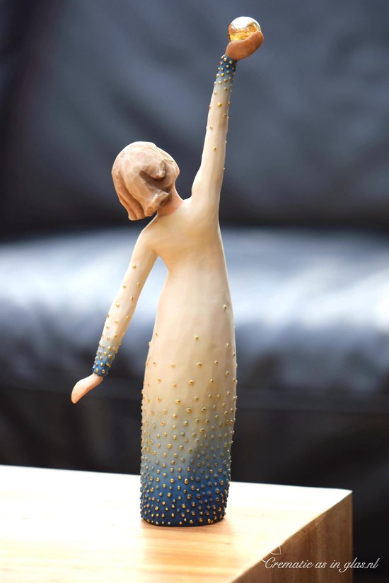 Een Willow Tree beeldje van een vrouw in een witte jurk met gouden stippen, die een gouden bol omhoog houdt.