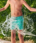Jongen in turquoise zwembroek met wit patroon, gespetterd met water.