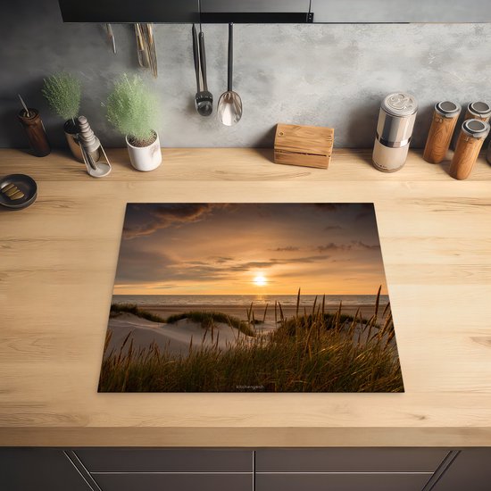 Inductiebeschermer met duinenlandschap bij zonsondergang op een houten aanrecht.