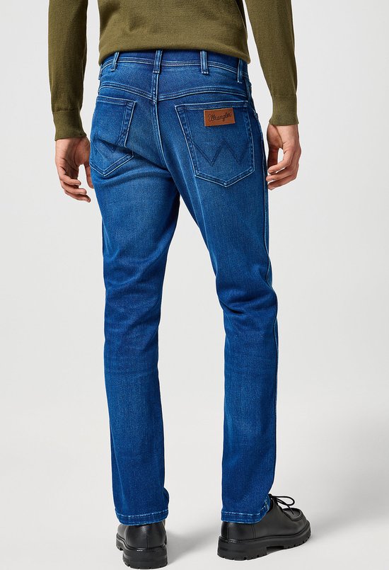 Achterkant van slanke blauwe jeans met licht vervaagd effect en bruin Wrangler logo.