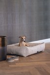 Italiaanse windhond in een lichtgrijze, ribstof hondenmand op een houten vloer.