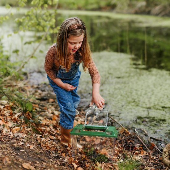 Meisje met spijkerbroek en bruine top doet een insectenkamer open bij een sloot.