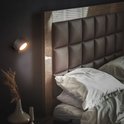 Zwarte wandlamp met warme verlichting, bevestigd aan een muur naast een bed.